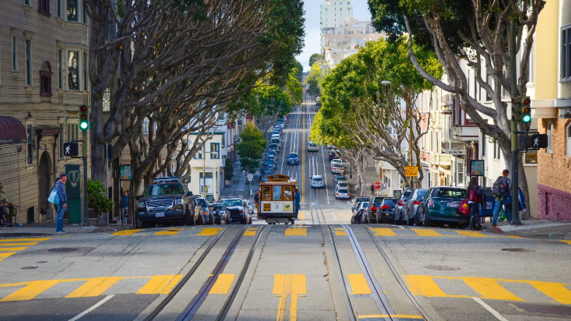 A wavy street with cars and a train cart along it, with trees and buildings on either side