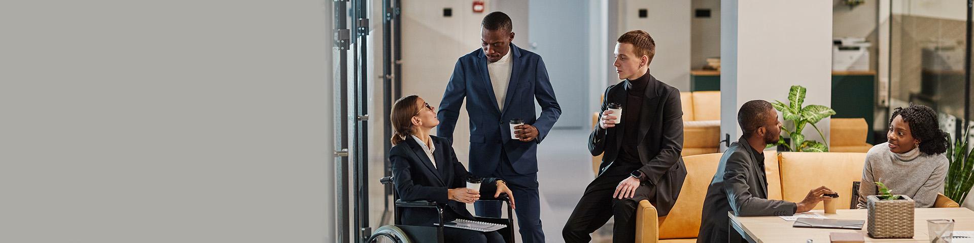 A diverse group of coworkers sit and chat in a lounge space in an office.